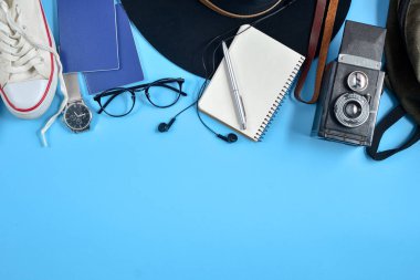 Retro kamera, şapka, sırt çantası, gözlük, saat, kalem, pasaport, Ayakkabı ve Not Defteri ile mavi arka plan üzerinde seyahat aksesuarları. Seyahat ya da tatil kavramı. Düz yatıyordu, en iyi görünüm. Yaz arka plan.