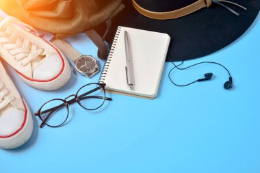 Şapka, sırt çantası, gözlük, saat, kalem, Ayakkabı ve Not Defteri ile mavi arka plan üzerinde düz yatıyordu seyahat aksesuarları. Görünümü en çok, uzay kopyalayın. Seyahat ya da tatil kavramı.