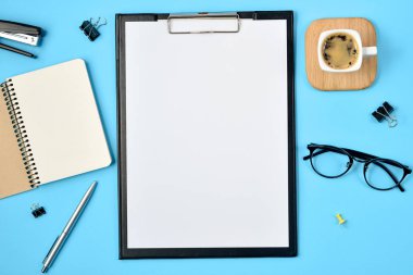 Çalışma alanı boş klibi kurulu, büro malzemeleri, kalem, kahve fincanı, not defteri, zımba ve mavi zemin üzerine gözlük ile alay. Düz yatıyordu, en iyi görünüm, kopya alanı