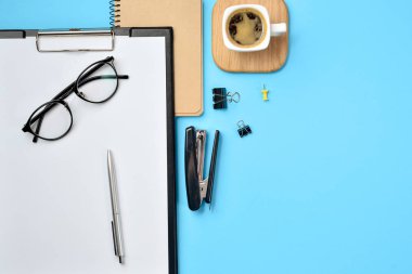 Çalışma alanı boş klibi kurulu, büro malzemeleri, kalem, kahve fincanı, not defteri, zımba ve mavi zemin üzerine gözlük ile alay. Düz yatıyordu, en iyi görünüm, kopya alanı