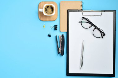 Düz yatıyordu, en iyi görünümü office tablo Resepsiyon. Çalışma alanı boş klibi kurulu, not defteri, gözlük, büro malzemeleri, Zımba, kalem ve kahve Kupası üzerinde mavi arka plan ile. Blog kavramı