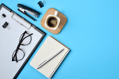 Office çalışma alanı boş klibi kurulu, büro malzemeleri, kalem, not defteri, gözlük, Zımba, kahve fincanı ve mavi arka plan üzerine gözlük ile. Düz yatıyordu, en iyi görünüm, şık konsept