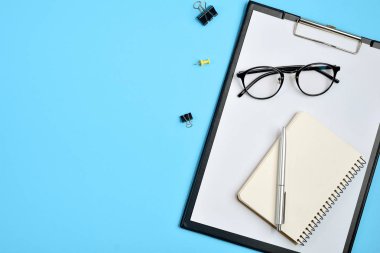 Office çalışma alanı boş klibi kurulu, büro malzemeleri, kalem, not defteri, gözlük mavi arka plan ile. Düz yatıyordu, en iyi görünüm, şık konsept