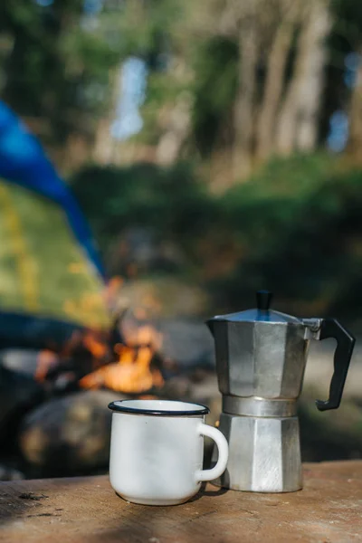 Maquette de tasse en aluminium de camping en métal ou tasse et cafetière près du feu de joie sur la tente de fond. Aventures conceptuelles et mode de vie nomade — Photo