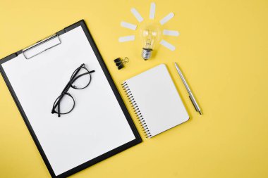 Çalışma masası tarzı tasarım ofis malzemeleri üst görünümü kalem, Not defteri, Gözlük, sarı bir arka planda ampul. Konsept beyin fırtınası ve yeni fikir