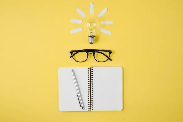 平面布局, 顶部视图, 复制空间。财务规划桌面与笔, 记事本, 眼镜和灯泡在黄色背景。概念头脑风暴和新想法 — 图库照片