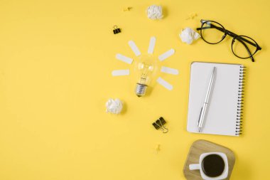 Boş klip panosu, ofis malzemeleri, kalem, Not defteri, Gözlük, kahve bardağı ve sarı arka planda ampul ile Office çalışma alanı. Konsept beyin fırtınası ve yeni fikir