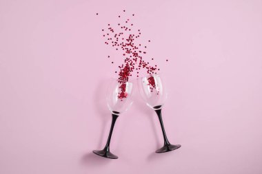 İki clinking şarap gözlükleri pembe renkli kağıt arka planda kırmızı kalp konfeti döktü. Minimal stil. Şablon kadınsı blog sosyal medya kartpostal
