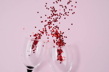 İki clinking şarap gözlükleri pembe renkli kağıt arka planda kırmızı kalp konfeti döktü. Minimal stil. Şablon kadınsı blog sosyal medya kartpostal