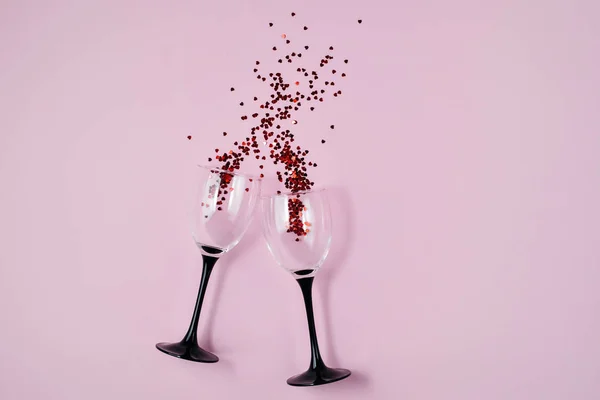 Twee champagneglazen met rode hart confetti op roze kleur papier achtergrond minimale stijl. Vakantie en creatief concept. Platte lay, bovenaanzicht, kopieerruimte — Stockfoto