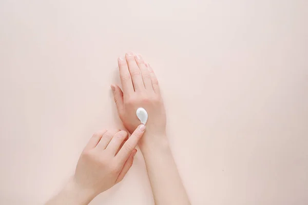 Woman moisturizing her hand with cosmetic cream lotion with copy space on a beige background. Beauty cosmetic research and development concept. Top view