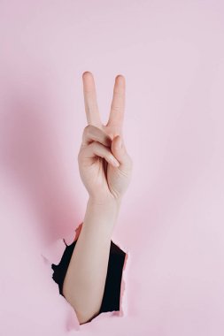 Pembe kağıt bir delik üzerinden görülebilir zafer işareti ile Kadın göstermek eller. Vücut dili kavramı.