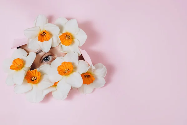 Close up of a female eye that looking is seen through a hole in torn pink paper with flowers. Beauty salon advertising with copy space. Creative and fashion concept.