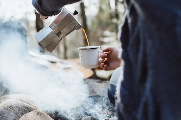 As mãos femininas vazam-se o café quente em uma floresta perto da fogueira. Menina sentada e segurando uma caneca de café depois de caminhar. Conceito de aventura — Fotografia de Stock