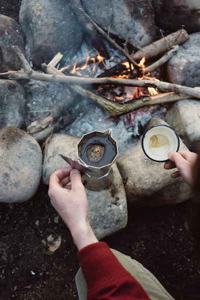 Homme randonneur se verse café chaud près de feu de joie. Homme assis et tenant une tasse de café après la randonnée. Concept d'aventure — Photo