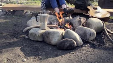 Kamp yapan kadın şenlik ateşinin yanında oturur ve kahve yapıyor. Doğal ormanda kız tatil seyahat macera doğa zevk.