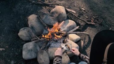 Şapkalı gezgin kadın şenlik ateşine yakın dağlarda sıcak içecek döker. Genç kadın yürüyüşten sonra oturup bir fincan kahve tutuyor. Tatil Konsepti