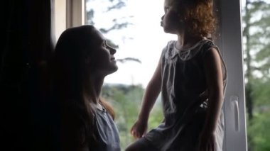 Sevimli anne gülerek pencerenin yanında oturan sevimli çocuk kızı ile burunokarak, mutlu anne ve küçük çocuk kız birlikte eğlenceli oynarken eğlenmek sarılma