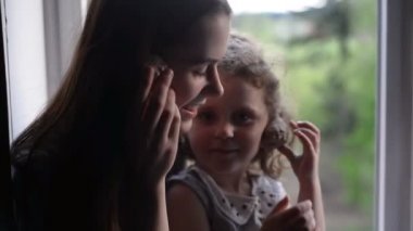 Young mommy and kid daughter  listen and playing seashell having fun  at home near the window, young mum and child enjoy spending time laughing together