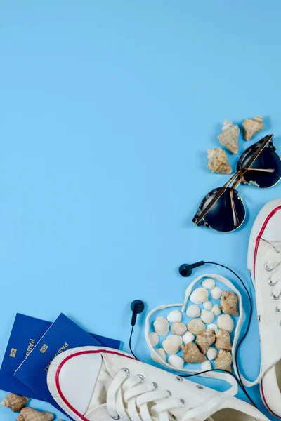 Traveler accessories. White footwear, two passport, eyeglasses and seashells on blue background with empty space for text. Travel vacation concept. Summer background. Flat lay, top view.
