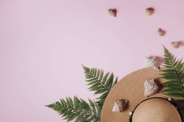 Yaz geçmişi. Gezgin aksesuarları, tropikal eğrelti otu yaprağı dalları, şapka ve pembe arka plan üzerinde deniz kabuğu. Seyahat tatil konsepti. Düz döşeme, üst görünüm, kopyalama alanı