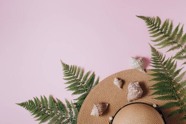 Gezgin aksesuarları, tropikal eğrelti otu yaprağı dalları, şapka ve pembe arka plan üzerinde deniz kabuğu. Seyahat tatil konsepti. Yaz geçmişi. Düz döşeme, üst görünüm, kopyalama alanı