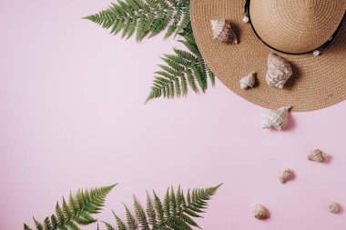 Gezgin aksesuarları, tropikal eğrelti otu yaprağı dalları, şapka ve pembe arka plan üzerinde deniz kabuğu. Seyahat tatil konsepti. Yaz geçmişi. Düz döşeme, üst görünüm, kopyalama alanı