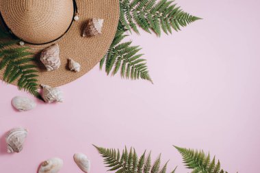 Yaz geçmişi. Gezgin aksesuarları, tropikal eğrelti otu yaprağı dalları, şapka ve pembe arka plan üzerinde deniz kabuğu. Seyahat tatil konsepti. Düz döşeme, üst görünüm, kopyalama alanı