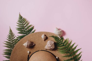 Gezgin aksesuarları, tropikal eğrelti otu yaprağı dalları, şapka ve pembe arka plan üzerinde deniz kabuğu. Seyahat tatil konsepti. Yaz geçmişi. Düz döşeme, üst görünüm, kopyalama alanı