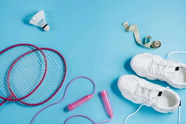 Sport flat lag met shuttle en badminton racket, springtouw, sneakers en het meten van tape op blauwe achtergrond. Fitness, sport en gezond lifestyle concept. — Stockfoto