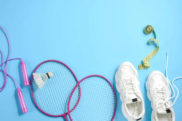 Sport flat lag met shuttle en badminton racket, springtouw, sneakers en het meten van tape op blauwe achtergrond. Fitness, sport en gezond lifestyle concept. — Stockfoto