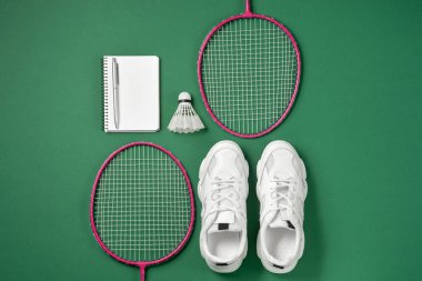 Sports equipment. Shuttlecock and badminton racket, sneakers, pen and notepad on green background. Fitness and healthy lifestyle concept. Flat lay, top view, copy space clipart
