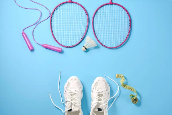 Sport flat lag met shuttle en badminton racket, springtouw, sneakers en het meten van tape op blauwe achtergrond. Fitness, sport en gezond lifestyle concept. — Stockfoto