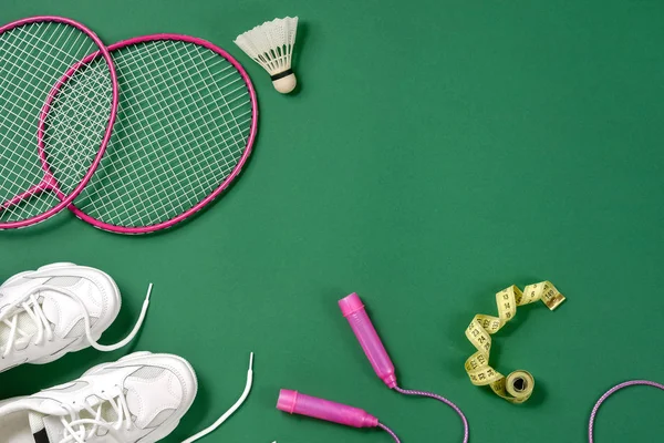 Sport flat lag met shuttle en badminton racket, springtouw, sneakers en het meten van tape op groene achtergrond. Fitness, sport en gezond lifestyle concept. — Stockfoto