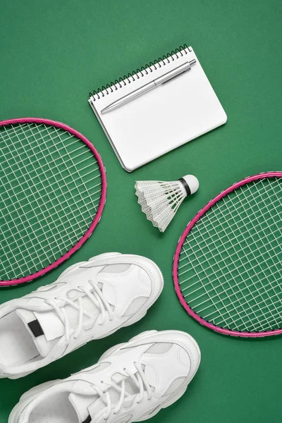 Sportartikelen. Shuttle en badminton racket, Sneakers, pen en Kladblok op groene achtergrond. Fitness en gezond lifestyle concept. Platte lay, bovenaanzicht, kopieerruimte — Stockfoto