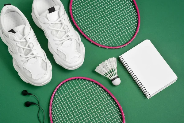 Sportartikelen. Shuttle en badminton racket, Sneakers, hoofdtelefoon, pen en Kladblok op groene achtergrond. Fitness en gezond lifestyle concept. Platte lay, bovenaanzicht, kopieerruimte — Stockfoto