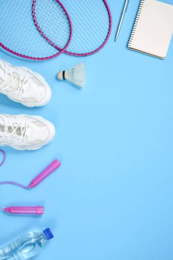 Sports flat lay with shuttlecock and badminton racket, skipping rope, sneakers, bottle water, pen and notepad on blue background. Fitness, sport and healthy lifestyle concept. clipart