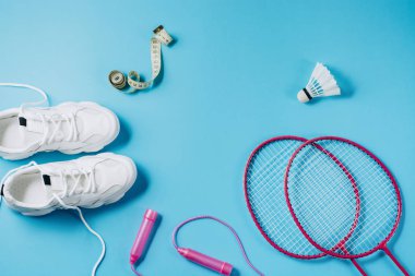 Spor düz mekiği ve badminton raket ile yatıyordu, halat atlama, spor ayakkabıları ve mavi arka planda ölçüm bandı. Fitness, spor ve sağlıklı yaşam konsepti.