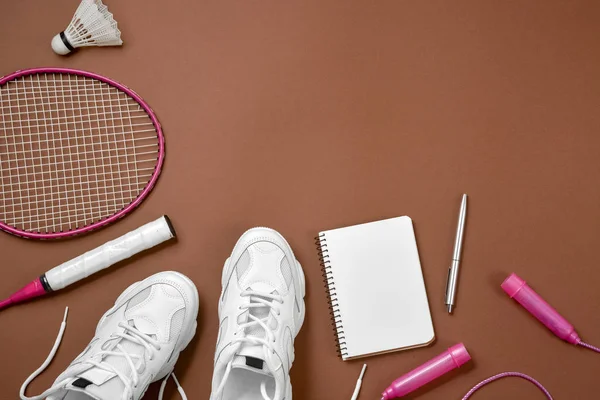 Sport flat lag met shuttle en badminton racket, springtouw, Sneakers, pen en Kladblok op bruine achtergrond. Fitness, sport en gezond lifestyle concept. — Stockfoto