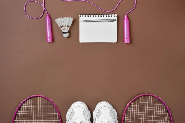 Sportartikelen. Shuttle en badminton racket, springtouw, Sneakers, pen en Kladblok op bruine achtergrond. Fitness en gezond lifestyle concept. Platte lay, bovenaanzicht, kopieerruimte — Stockfoto