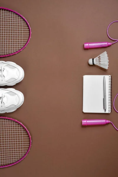 Deportivo plano con transbordador y raqueta de bádminton, saltar la cuerda, zapatillas, bolígrafo y bloc de notas sobre fondo marrón. Fitness, deporte y estilo de vida saludable . — Foto de Stock