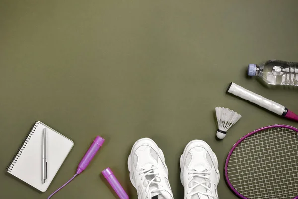 Sport uitrusting. Shuttle en badminton racket, springtouw, Sneakers, fles water, pen en Kladblok op groene achtergrond. Fitness en gezond lifestyle concept. Platte lay, bovenaanzicht, kopieerruimte — Stockfoto