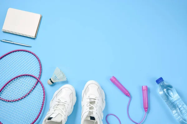 Sports plat avec navette et raquette de badminton, corde à sauter, baskets, bouteille d'eau, stylo et bloc-notes sur fond bleu. Concept de fitness, sport et mode de vie sain . — Photo