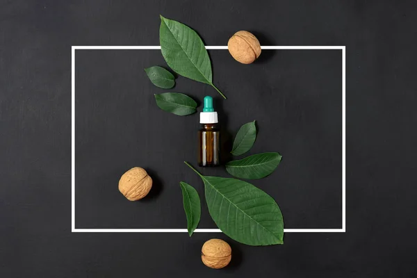 Natural Serums. Cosmetic and medicinal oil of walnut and white frame on black background. Flat lay, top view, copy space — Stock Photo, Image