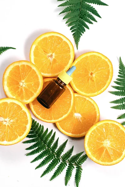 Natural cosmetic skincare serum packaging with leaf fern and fresh juicy orange fruit on white background. Beauty vitamin ingredient. alternative medicine. Flat lay, top view, copy space
