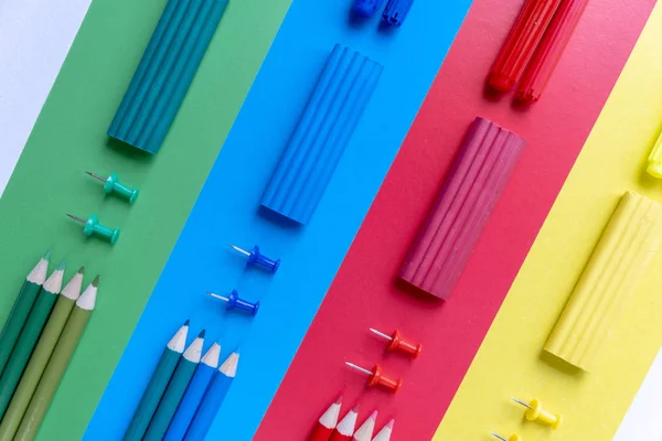 Creative flat lay back to school concept with colored pencils, plasticine and office supplies on blue, green, red and yellow background. Top view, copy space.
