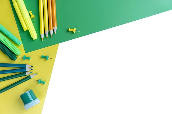 Вид зверху в'язання плоский настільний робочий стіл стилізований дизайнерським шкільним та офісним приладдям з кольоровими олівцями на білому, зеленому та жовтому тлі. Копіювати простір . — стокове фото