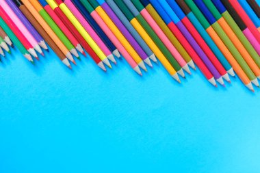 Okul konseptine geri dönelim. Mavi arka planda yalıtılmış birçok renkli kalemin yakın çekim görüntüleri. Düz döşeme, üst görünüm, kopyalama alanı.