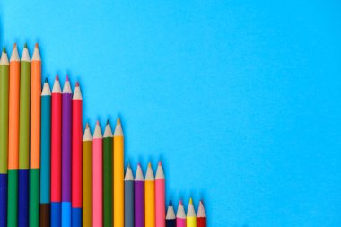 Okul konseptine geri dönelim. Mavi arka planda yalıtılmış birçok renkli kalemin yakın çekim görüntüleri. Düz döşeme, üst görünüm, kopyalama alanı.