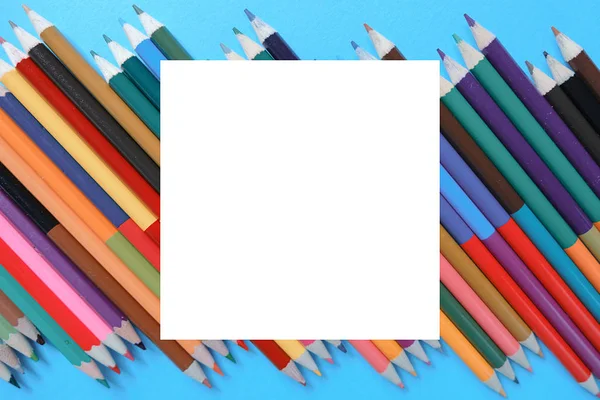 Concept scolaire avec crayons de couleur sur fond bleu avec cadre blanc. Pose plate créative, vue du dessus, espace de copie . — Photo
